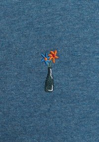 Geborduurd ontwerp op een blauw gestructureerde stof toont een zwarte fles met oranje en blauwe bloemen, wat een duidelijk kleurcontrast en detail laat zien.