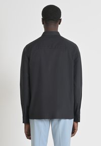 Schwarzes Langarmshirt mit geradem Schnitt, geknöpften Manschetten und einem Rückenausschnitt. Glattes, leichtes Material ohne sichtbare Muster oder Akzente.