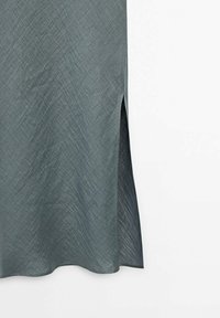 Robe fluide en tissu texturé et bleu canard atténué ; présente une fente latérale pour faciliter les mouvements ; silhouette douce et apparence légère.