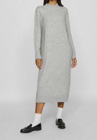 Robe gris tricotée à manches longues, col et ourlet côtelés. Stylisée avec des mocassins noirs et des chaussettes blanches. Texture lisse et longueur midi.