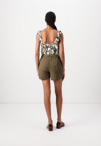 Top con motivo floreale e spalline arricciate, abbinato a pantaloncini verde oliva. L'outfit presenta una vestibilità rilassata e un tessuto strutturato.