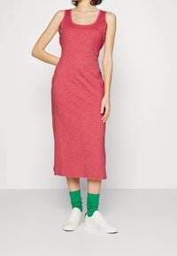 Lång, figurnära tankklänning i melerat rosa tyg. Har en rund halsringning och en knälång fåll. I kombination med vita sneakers och gröna ribbade strumpor.