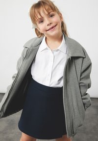 Harmaa vetoketjullinen takki, valkoinen napillinen paita, jossa on tasku, tummansiniharmaa hame. Ominaisuudet: pehmeä rakenne, yksinkertainen muotoilu ja vaatimaton pituus.