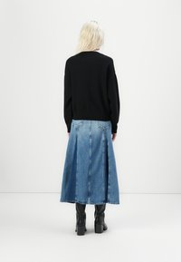 Schwarzer Strickpullover mit langen Ärmeln, kombiniert mit einem blauen Denimrock mit knielanger Länge und seitlichen Schlitzen, getragen mit schwarzen High-Heels-Stiefeln.