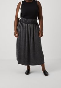 Svart linne, grå denim maxikjol med smockad midja, och svarta slip-on skor. Slät textur, avslappnad design, ankellängd.