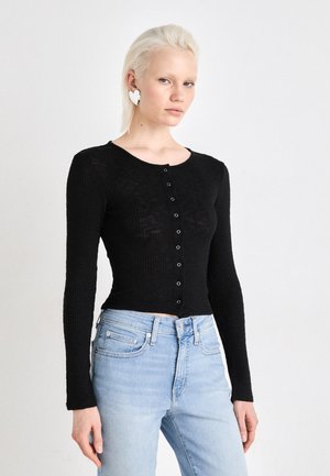 Schwarzes, geripptes Langarmoberteil mit Rundhalsausschnitt und Knopfdetail, kombiniert mit hellblauen, hoch taillierten Jeans. Glatte Textur, taillierte Passform.