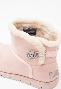 Bottine d'hiver en daim rose clair avec doublure en polaire crème, bouton décoratif argenté, et semelle en caoutchouc beige, vue de l'arrière en angle latéral.