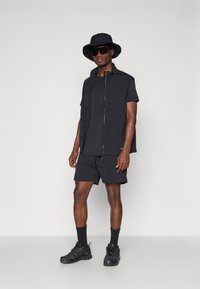 Black athletic outfit featuring a zip-up sleeveless jacket, t-shirt, shorts, and dark sneakers. Includes a bucket hat and sunglasses.