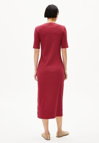 Rode, geribbelde midi-jurk met korte mouwen en een ronde hals. Zijsplits aan de zoom. Model draagt beige instappers.