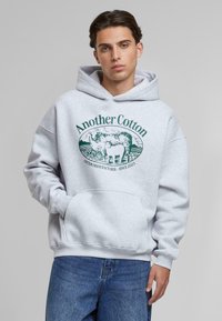 Gray hooded sweatshirt made of cotton, featuring a central green graphic with cows and text "Another Cotton" in a circular design.