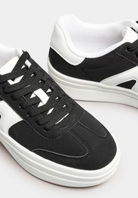 Svartvita sneakers med en slät syntetisk ovandel, rund tå, platta snörningar och en texturerad sula med en minimalistisk design.