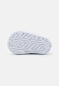 White rubber shoe sole with a textured surface featuring a herringbone pattern. Rounded edges and a slightly raised centerline are visible.