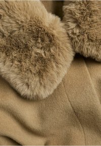 Beiger Wollmischstoff mit weichem Kunstpelzkragen. Glatte Textur mit feinem, leicht glänzendem Erscheinungsbild. Nahtdetails erkennbar.