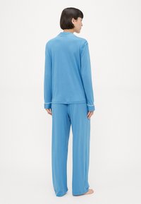Ανοιχτό μπλε σετ πιτζάμας με μακρυμάνικη μπλούζα με γιακά και παντελόνι φαρδύ, κατασκευασμένο από μαλακό ύφασμα με λευκές λεπτομέρειες.