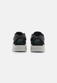 Nike Air tenisice, s gornjim dijelom od sive antilop kože i crne glatke kože, tamnoplave akcenti i teksturiranim bijelim potplatom.