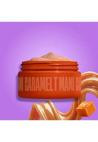 Open orange container labeled caramel with beige cream inside, caramel swirl and caramel piece against purple background.