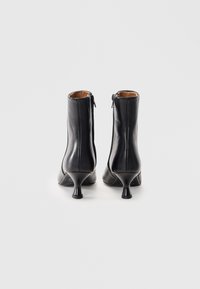 Bottines en cuir noir au design épuré, avec un bout pointu et un talon aiguille courbé, fermeture éclair à l'arrière, et texture lisse.