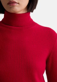 Roter Rollkragenpullover mit gerippter Textur. Das eng anliegende Design hebt den Halsbereich hervor und besteht aus einem Strickstoff.