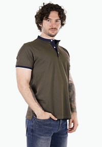 Polo shirt verde oliva con colletto blu scuro e strisce bianche accentate sulle maniche. Presenta una chiusura con bottoni a tre e un design aderente.