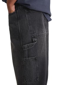 Czarne dżinsy o luźnym kroju, z wieloma kieszeniami, widocznymi detalami przeszycia oraz miękkim, lekko teksturowanym wykończeniem.