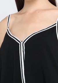 Top in tessuto nero con piping bianco lungo il colletto e le spalline, design a forma di V e texture leggera.