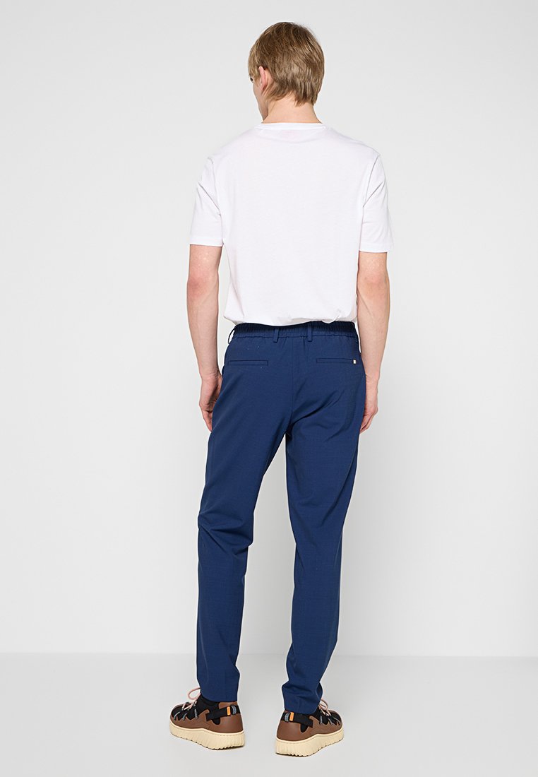 Granatowe spodnie o luźnym kroju, z elastycznym paskiem w talii i bocznymi kieszeniami. Model ma na sobie białą koszulkę i brązowe sneakersy.