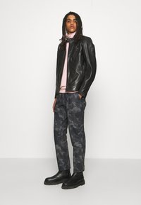 Black leather motorcycle jacket with a zip closure, pink turtleneck, and dark gray camo pants. Black chelsea boots with lug sole.
