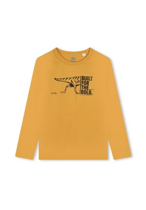 Langsleeve t-shirt in mosterdgeel, met een zwarte dinosaurusgrafiek en de tekst "GEBOUWD VOOR DE DAREDEVILS." Gladde katoenstof.