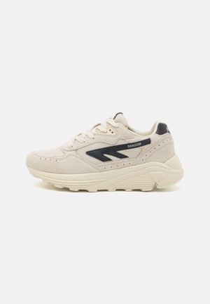 Kremowe zamszowe sneakersy z granatowymi akcentami i teksturowanymi panelami siateczkowymi. Posiadają grubą beżową podeszwę i wyraźne logo na boku.