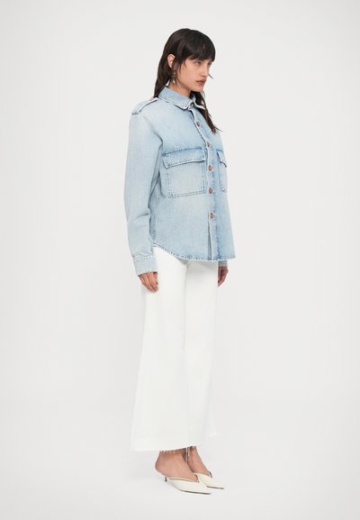 Ανοιχτό μπλε τζιν πουκάμισο με δύο μπροστινές τσέπες, κλείσιμο με κουμπιά και στρογγυλεμένο τελείωμα, συνδυασμένο με λευκό παντελόνι φαρδιάς γραμμής και μπεζ ψηλοτάκουνα.