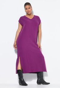 Vestido midi morado con escote en V y mangas cortas, con aberturas laterales; combinado con botas vaqueras negras para dar un contraste adicional.