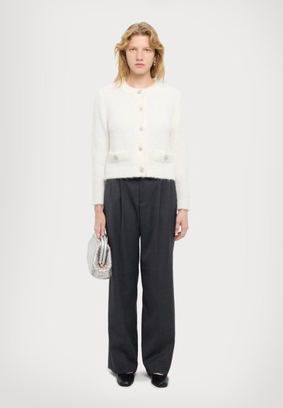 Weißer, flauschiger Cardigan mit sechs Knöpfen und zwei Fronttaschen, kombiniert mit dunkelgrauen, weit geschnittenen Hosen und einer silbernen Clutch.