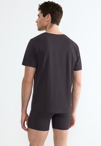 T-shirt a girocollo di colore grigio scuro e pantaloni corti coordinati. Realizzato in tessuto liscio, design aderente, maniche corte e cuciture minime. Nessun logo visibile.