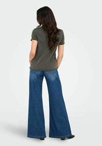 Camiseta de manga corta verde oliva combinada con pantalones vaqueros de denim azul de pierna ancha. La tela parece suave, con un corte relajado y detalles de costura sutiles.