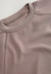 Lys mauve pullover med en glat tekstur, rund halsudskæring og raglanærmer. Har subtile stikninger og et mærke indeni.