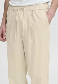 Beige bukser med elastisk liv med snor, sidelommer og en afslappet pasform. Lavet af glat, letvægtsmateriale med minimal tekstur.