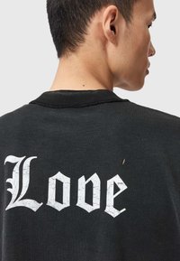 Fekete póló hófehér, repedezett "Love" grafikával a hátoldalon. Klasszikus gallérral és enyhe kopással a nyak környékén.