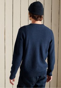 Pull texturé bleu marine avec un col rond, des poignets et un ourlet côtelés, accompagné d'un bonnet assorti, vu de dos.