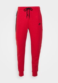 Röda Nike sweatpants av mjukt material, med en svart logotyp, dragsko i midjan, sidofickor med dragkedja och smalnande avslut.