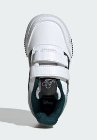 Sneaker bianca in pelle con dettagli verdi, doppie cinghie a strappo, suola nera texturizzata e marchio Disney con una grafica del personaggio sul tallone.