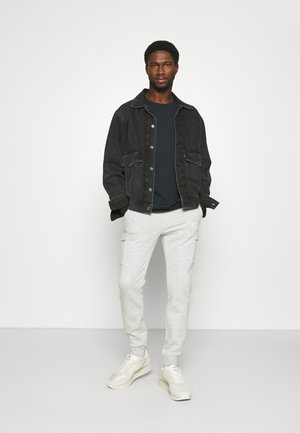 Black denim jacket over a dark shirt, paired with light gray sweatpants and beige sneakers. Features include pockets on the jacket and pants.