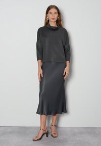 Grauer Schalkragenoberteil und dazu passende seidige Midirock, mit einem seitlichen Schlitz und Riemchenabsätzen. Glatte Textur mit einem eleganten Finish.