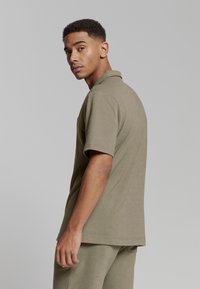 Olijfgroen polo-shirt met een zachte textuur, korte mouwen en een klassieke kraag; heeft een subtiele logodetail op de borst.