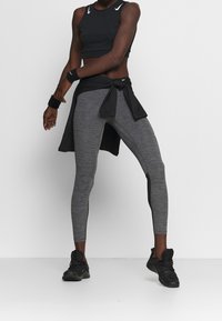 Svart sportcrop top, grå texturerade leggings med svarta sidopaneler, svart knytlager i midjan och svarta träningsskor.