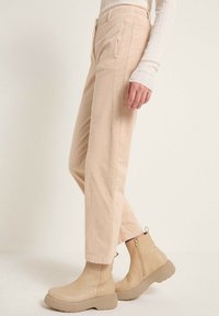 Ljust beige kordflorsbyxor med sidofickor, smal passform och sydda detaljer, tillsammans med matchande ankelstövlar med kraftig sula.