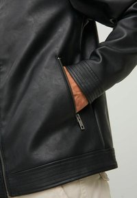 Giacca in ecopelle nera con tasca con zip, polsini a costine e una finitura liscia con dettagli sottili lungo l'orlo.