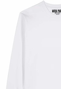 T-shirt blanc à manches longues et col rond avec l'inscription « MIRA PARK Born to Rock Organic Cotton » imprimée à l'intérieur du col.