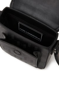 Borsa a tracolla in pelle nera con motivi in rilievo. L'interno presenta un'etichetta del marchio. Include compartimenti separati e una chiusura magnetica.