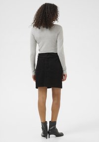 Jupe en velours côtelé noir à coupe droite, avec deux poches arrière et une taille. Associée à un haut à manches longues gris clair et des bottines noires.