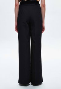 Höga svarta vida byxor med en slät tygfinish, som har veck för struktur och ett elastiskt midjeband för komfort.